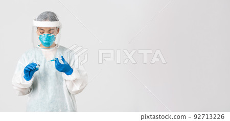 Covid-19, coronavirus disease, healthcare workers concept. Serious-looking female physician, asian doctor in personal protective equipment insert syringe in ampoule with vaccine, white background Covid-19, coronavirus disease, healthcare workers concept. Serious-looking female physician, asian doctor in personal protective equipment insert syringe in ampoule with vaccine, white background 92713226
