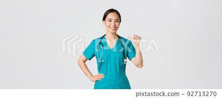 Covid-19, healthcare workers, pandemic concept. Professional confident female asian doctor, nurse in scrubs pointing at herself and smiling, guarantee she knows what do, white background 92713270
