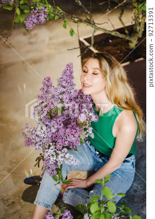 a blonde woman in a green top and jeans with lilac flowers. a blonde woman in a green top and jeans with lilac flowers. 92713391