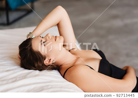 an attractive brunette woman in a black bodysuit by the bed in the bedroom.  92713445