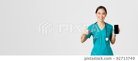 Covid-19, healthcare workers and online medicine concept. Portrait of young asian female physician, doctor in scrubs show thumbs-up and smartphone screen, promote application, white background 92713749