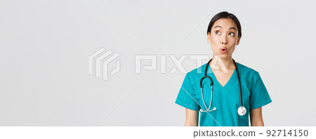 Healthcare workers, preventing virus, quarantine campaign concept. Impressed and amazed asian female doctor, nurse in medical scrubs looking upper left corner pleased, white background 92714150