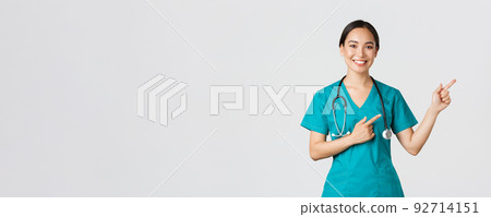 Covid-19, healthcare workers, pandemic concept. Smiling beautiful asian female nurse, intern pointing fingers upper right corner, inviting for checkup, online clinic appointment, white background 92714151