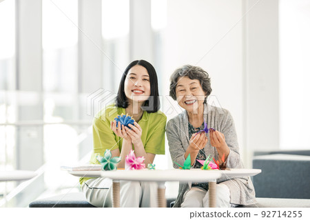Portrait of caregiver and senior woman folding origami Portrait of caregiver and senior woman folding origami 92714255