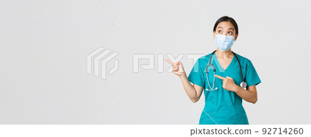 Covid-19, coronavirus disease, healthcare workers concept. Excited and amazed asian female doctor, physician in medical mask and gloves, pointing fingers upper left corner, white background 92714260