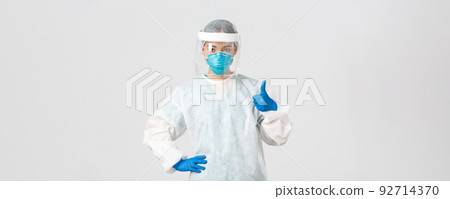 Covid-19, coronavirus disease, healthcare workers concept. Serious-looking professional female asian doctor in personal protective equipment, showing thumb-up, ensure safety of patient 92714370