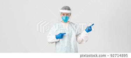 Covid-19, coronavirus disease, healthcare workers concept. Professional female doctor, tech lab employee in personal protective equipment pointing fingers right, showing way, white background Covid-19, coronavirus disease, healthcare workers concept. Professional female doctor, tech lab employee in personal protective equipment pointing fingers right, showing way, white background 92714895
