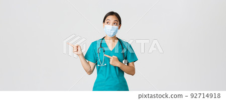 Covid-19, coronavirus disease, healthcare workers concept. Excited and amazed asian female doctor, physician in medical mask and gloves, pointing fingers upper left corner, white background 92714918