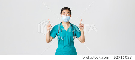 Covid-19, coronavirus disease, healthcare workers concept. Intrigued and excited asian woman doctor, nurse in medical mask and gloves, looking and pointing fingers up, white background Covid-19, coronavirus disease, healthcare workers concept. Intrigued and excited asian woman doctor, nurse in medical mask and gloves, looking and pointing fingers up, white background 92715058