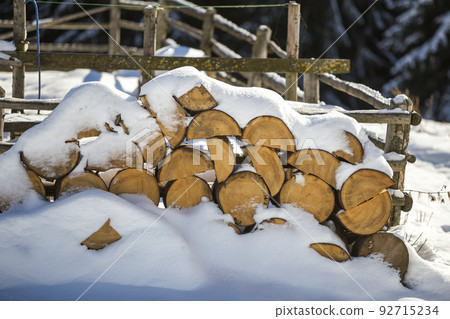 Neatly piled stack of chopped dry trunks wood covered with snow outdoors on bright cold winter sunny day, abstract background, Fire wood logs prepared for winter, ready for burning. 92715234