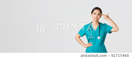 Covid-19, healthcare workers, pandemic concept. Exhausted and bothered, annoyed asian female doctor, nurse making shot gun gesture over head from boredom, white background 92715468