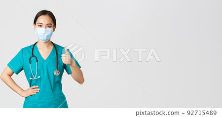 Covid-19, coronavirus disease, healthcare workers concept. Confident smiling asian doctor, female nurse or physician in medical mask and scrubs, show thumbs-up assure quality, guanratee service Covid-19, coronavirus disease, healthcare workers concept. Confident smiling asian doctor, female nurse or physician in medical mask and scrubs, show thumbs-up assure quality, guanratee service 92715489