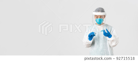 Covid-19, coronavirus disease, healthcare workers concept. Serious-looking female physician, asian doctor in personal protective equipment insert syringe in ampoule with vaccine, white background 92715518