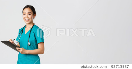 Healthcare workers, preventing virus, quarantine campaign concept. Smiling cute asian female nurse, intern in scrubs, writing on clipboard, fill-in papers, looking a camera pleased, white background 92715587