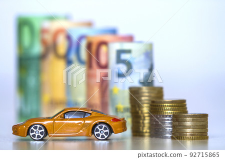 Blurred row of rolled hundred, fifty, twenty, ten and five new euro banknotes and pile of coins with yellow toy expensive sport car. Symbol of financial prosperity, vehicle sale and purchase. 92715865