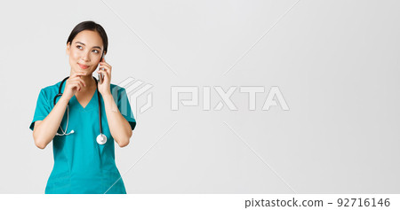 Covid-19, healthcare workers and preventing virus concept. Portrait of smiling asian female doctor, intern in scrubs talking on phone and looking thoughtful, thinking or making choice Covid-19, healthcare workers and preventing virus concept. Portrait of smiling asian female doctor, intern in scrubs talking on phone and looking thoughtful, thinking or making choice 92716146