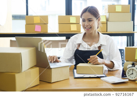 Asian businesswoman Start up small business owner writing address on cardboard box a. Asian businesswoman Start up small business owner writing address on cardboard box a. 92716167
