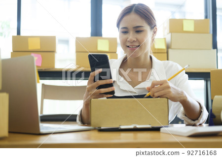 Asian businesswoman Start up small business owner writing address on cardboard box a. Asian businesswoman Start up small business owner writing address on cardboard box a. 92716168