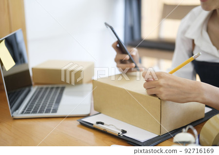 Close up Young Asian businesswoman start up small business owner writing address on cardboard box a. Close up Young Asian businesswoman start up small business owner writing address on cardboard box a. 92716169
