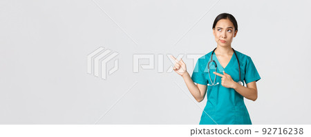 Covid-19, healthcare workers, pandemic concept. Skeptical and doubtful pretty asian doctor, nurse in scrubs smirk, pointing upper left corner, looking with reluctant hesitant face, white background Covid-19, healthcare workers, pandemic concept. Skeptical and doubtful pretty asian doctor, nurse in scrubs smirk, pointing upper left corner, looking with reluctant hesitant face, white background 92716238