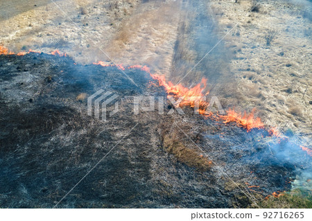 Aerial view of grassland field burning with red fire during dry season. Natural disaster and climate change concept Aerial view of grassland field burning with red fire during dry season. Natural disaster and climate change concept 92716265