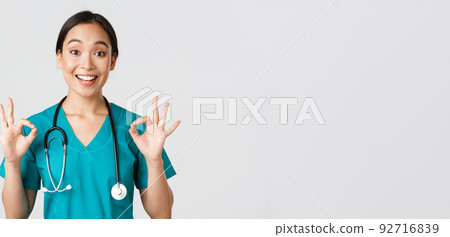 Healthcare workers, preventing virus, quarantine campaign concept. Excited and pleased asian female doctor, nurse in scrubs with stethoscope, showing okay gesture, white background 92716839