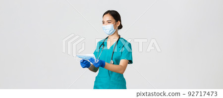 Covid-19, coronavirus disease, healthcare workers concept. Smiling friendly female nurse, physician in scrubs and rubber gloves provide patients with medical masks, white background 92717473