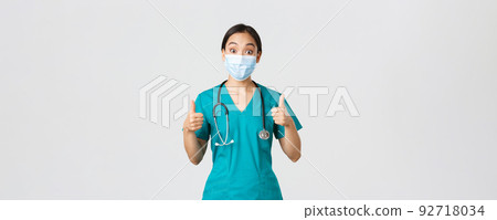 Covid-19, coronavirus disease, healthcare workers concept. Impressed happy asian female doctor, physician in medical mask and scrubs show thumbs-up, agree, compliment choice, praise nice work 92718034