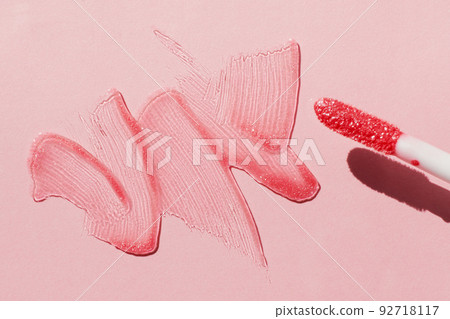 Smears of shining lip gloss and lip gloss brush on pink background, hard shadows 92718117