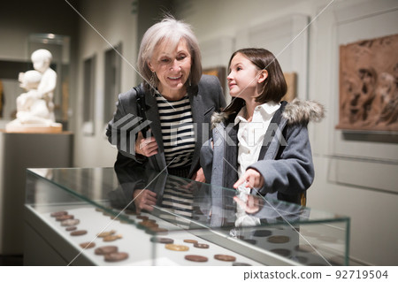 Aged female tutor with preteen girl exploring showpieces in museum Aged female tutor with preteen girl exploring showpieces in museum 92719504