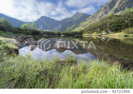 Alpine peaks reflected in small still tarn along with green foliage, Slovakia, Europe Alpine peaks reflected in small still tarn along with green foliage, Slovakia, Europe 92722998