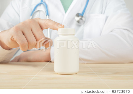 doctor holding white bottle of tablets or pills with a blank white label for treatment of an illness or injury. Doctor's appointment blank pills bottle. doctor holding white bottle of tablets or pills with a blank white label for treatment of an illness or injury. Doctor's appointment blank pills bottle. 92723970