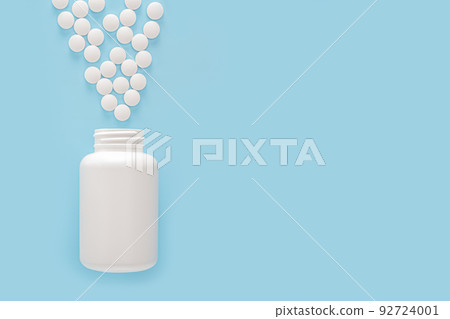 Scattered medicine pills and white container at blue background with copy space. pharmaceutical medicine pills, tablets and bottle top view 92724001