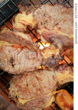 Close-up shot grilling the meat steak on the iron grill over the fire. Cooking a meat barbeque Close-up shot grilling the meat steak on the iron grill over the fire. Cooking a meat barbeque 92724419
