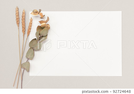 White invitation card mockup with a dried eucalyptus and golden ears decoration on a neutral table. 5x7 ratio, similar to A6, A5. minimalistic design 92724648