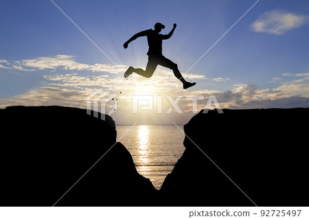 Silhouette of man jumping over the cliff on sunrise background, achievement business concept 92725497