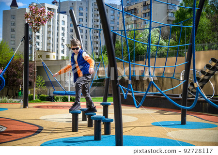 Children's obstacle course on a modern playground. Kid crossing a wooden bridge or other barriers using his body balance. Development of the child's agility and courage 92728117