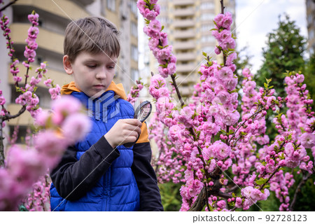 Little boy looking at flower through magnifier. Charming schoolb Little boy looking at flower through magnifier. Charming schoolb 92728123