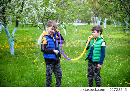 Colorful anti-stress fidget push pop tube toys for children. Flexible corrugated pipe in kids hands. Two Boys playing with sensory toys. Fun playing for developing imagination and fine motor skills 92728243