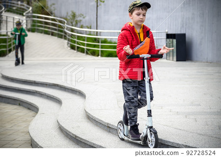 Happy family lifestyle and holiday concept. little boy and his sibling brother riding scooters, walking in city, street. Having fun 92728524
