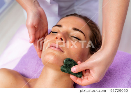 Relaxing massage. European woman getting quartz guache face massage in spa salon, side view 92729060