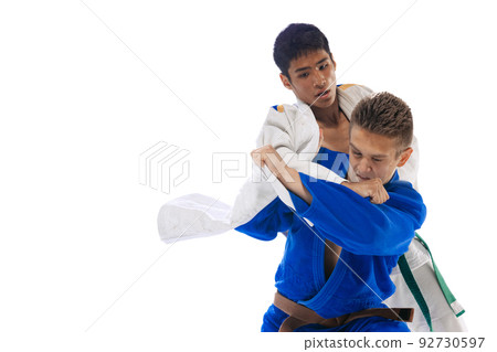 Dynamic portrait of two young men, professional judo athletes training, fighting isolated over white background 92730597