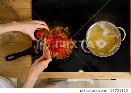 Closeup overhead view of female hand adding canned peeled tomatoes into frying pan while preparing sauce Closeup overhead view of female hand adding canned peeled tomatoes into frying pan while preparing sauce 92731120