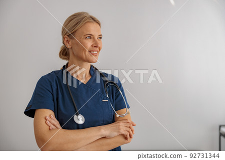 Smiling professional woman doctor with stethoscope on her workplace in hospital looking side Smiling professional woman doctor with stethoscope on her workplace in hospital looking side 92731344