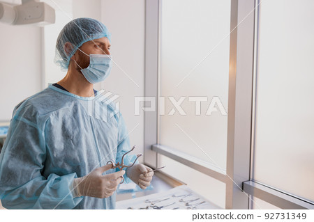 Professional doctor surgeon holding scalpel and forceps in operation room and looking away 92731349