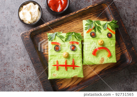 Children's food green burrito sandwich with a funny face on a wooden tray. horizontal top view Children's food green burrito sandwich with a funny face on a wooden tray. horizontal top view 92731565
