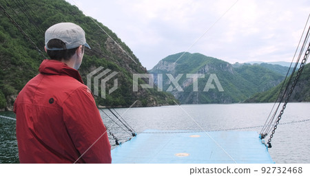 Unrecognizable traveler moving on turquoise lake in summer mountains on ferry. Man looks at scenic mountains of sailing ship. Water travel. Getaway, recreation tourism. Beautiful trip in Albania Alps Unrecognizable traveler moving on turquoise lake in summer mountains on ferry. Man looks at scenic mountains of sailing ship. Water travel. Getaway, recreation tourism. Beautiful trip in Albania Alps 92732468
