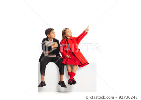 Portrait of two children, boy and girl in stylish autumn clothes sitting, pointing upwards isolated over white background 92736245