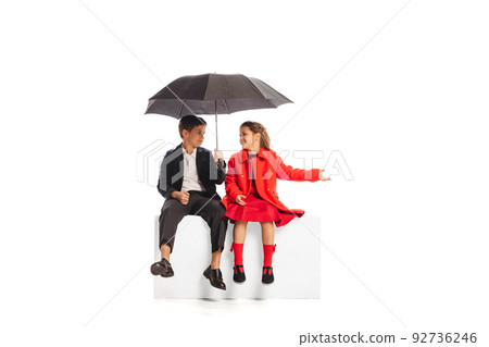 Portrait of boy and girl, children sitting under umbrella, talking isolated over white studio background Portrait of boy and girl, children sitting under umbrella, talking isolated over white studio background 92736246