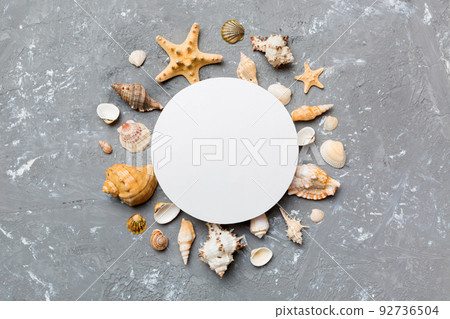 Summer time concept with blank greeting card and blank white paper on colored background. Seashells from ocean shore in the shape of frame separated with space for text top view Summer time concept with blank greeting card and blank white paper on colored background. Seashells from ocean shore in the shape of frame separated with space for text top view 92736504